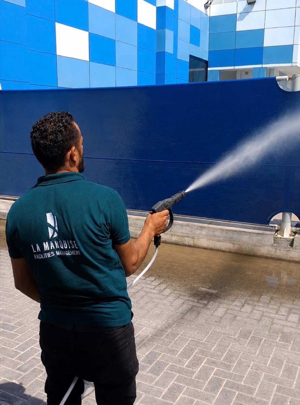 La Marquise Facilities Management technician pressure-washing a building exterior